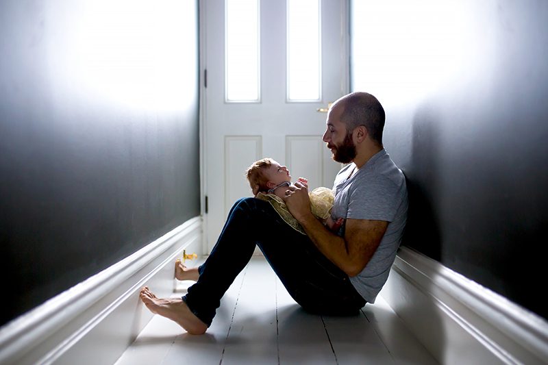 Newborn Photography - a dad sits in a hallway with his baby girl in his lap