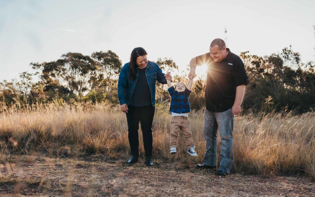 Parents hoist their giggling son into the air as the sun sets behind them