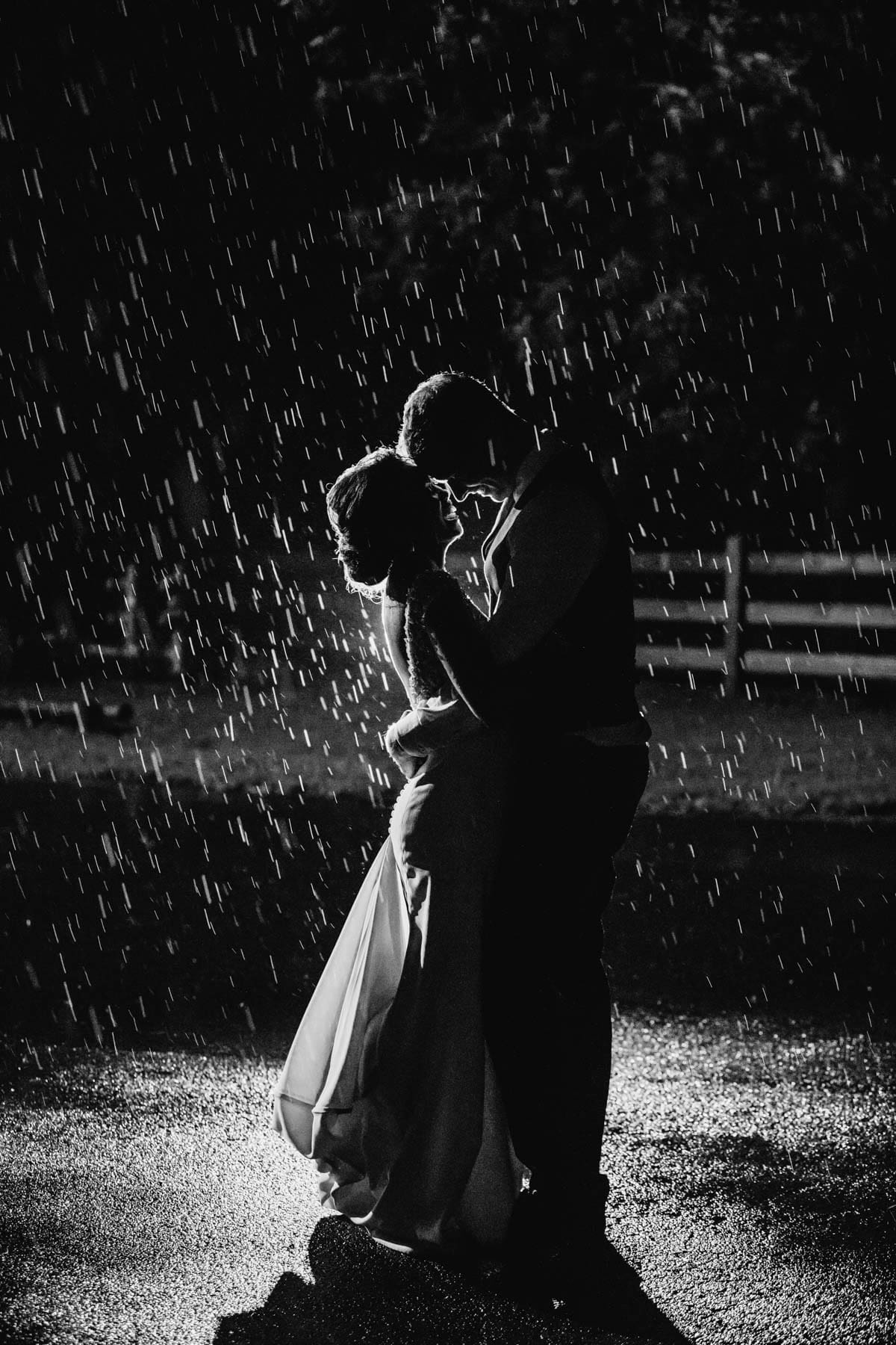 BW-Sydney-Wedding-Photographer-Elysium-Photography-J&M-650 A married couple stand in the rain at night, cuddling and laughing at Gledswood Estate