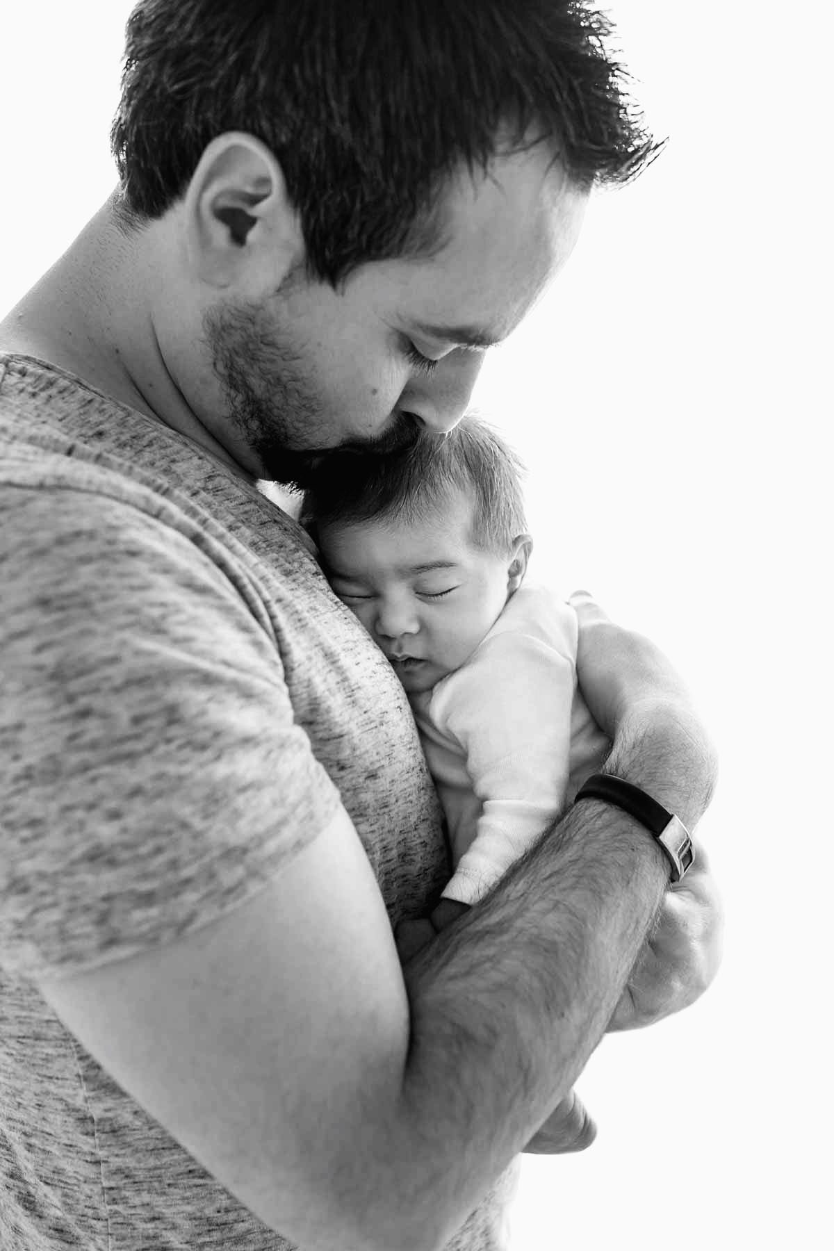 A father hold his baby girl to his chest as he kisses the top of her head