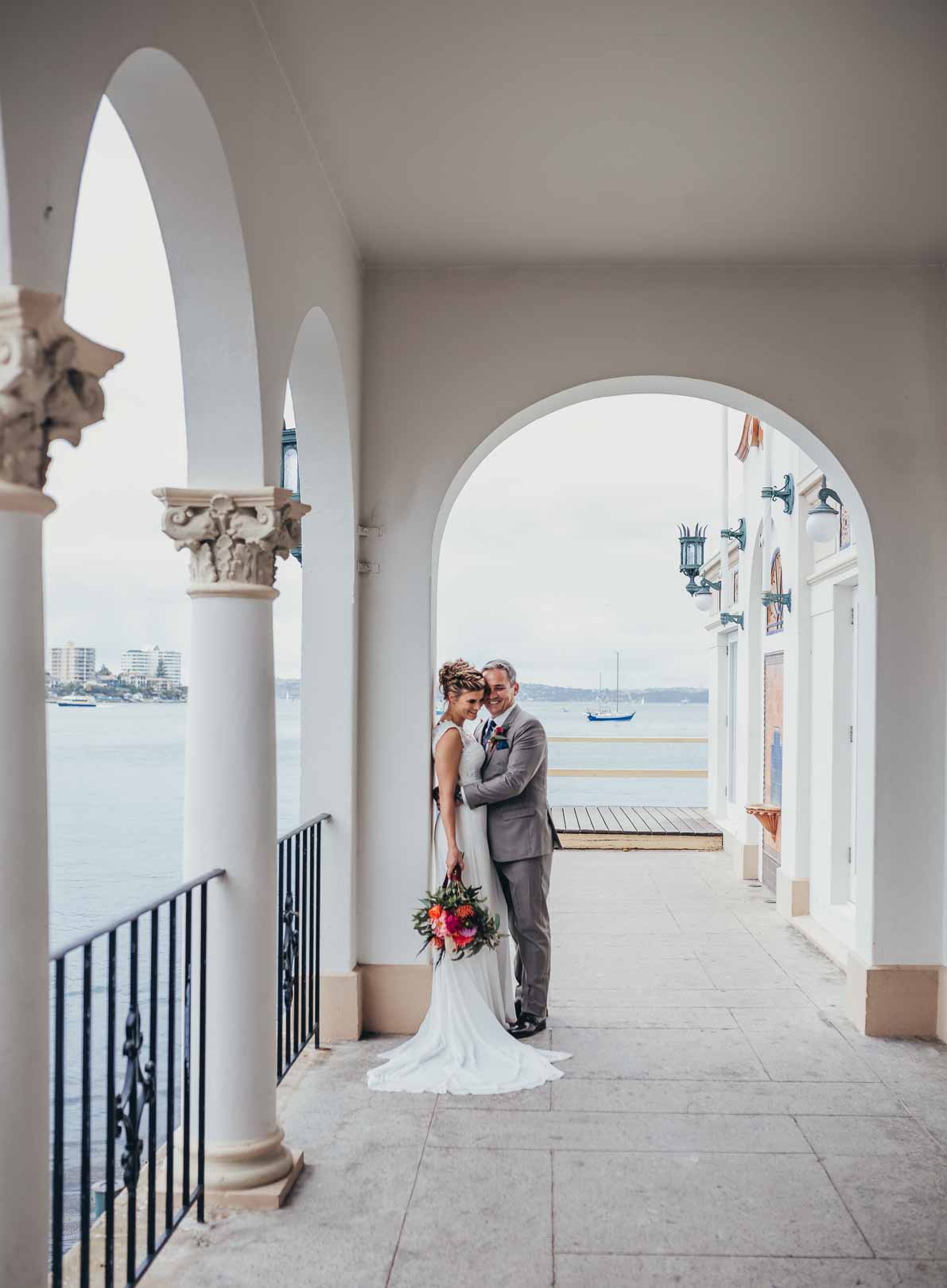 Couple stand cuddling at Manly Pavilion before their wedding ceremony