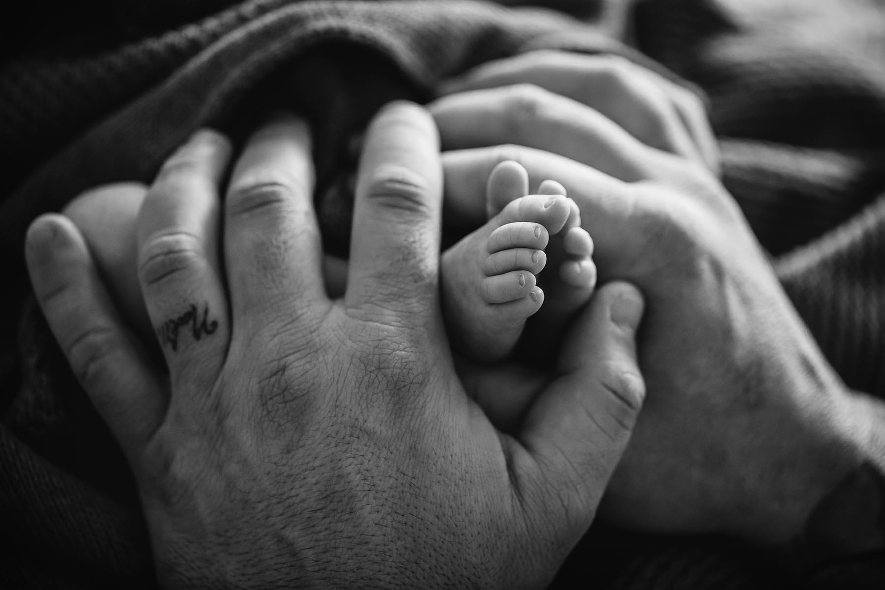 Black and white photograph showing the contrast between dads rough hands and soft newborn feet