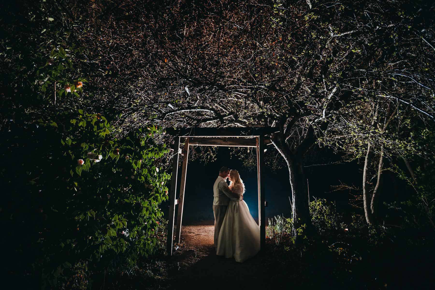 A night photograph of a married couple standing under the wedding arch