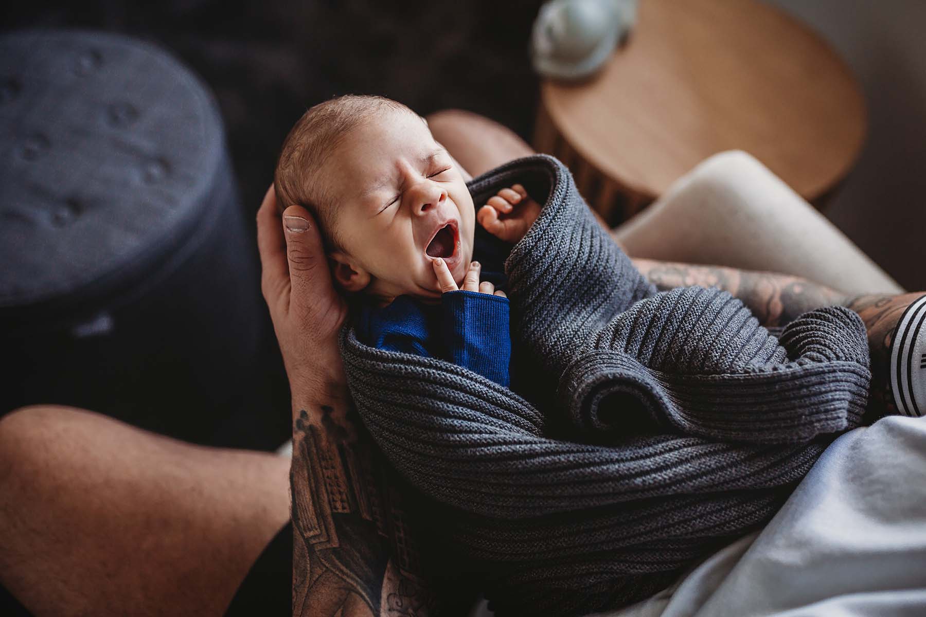 A wrapped newborn baby yawns, laying in dads hands