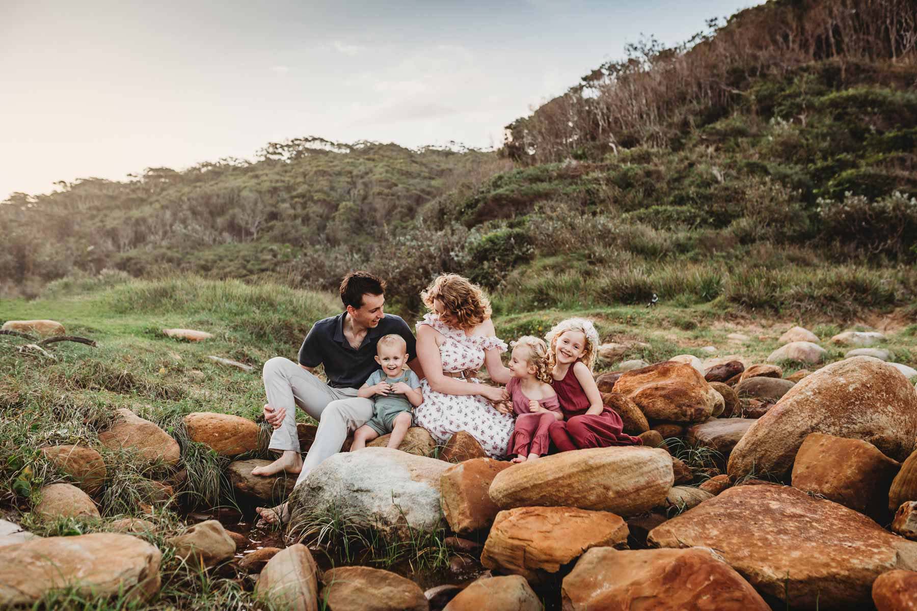 A family sitting on beach rocks cuddle together and giggle with each other