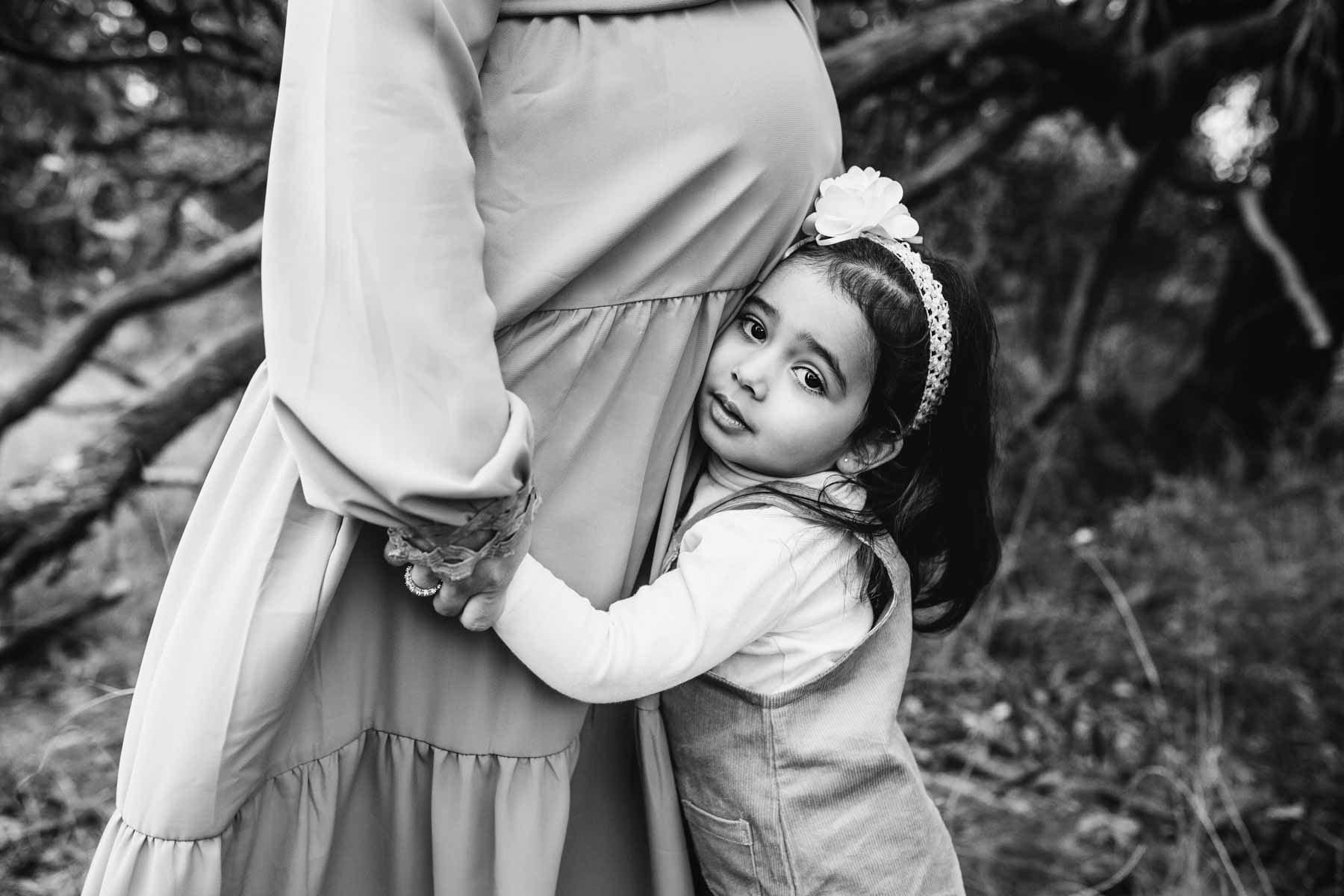 Black and white photograph, a little girl cuddles her mamma's pregnant belly