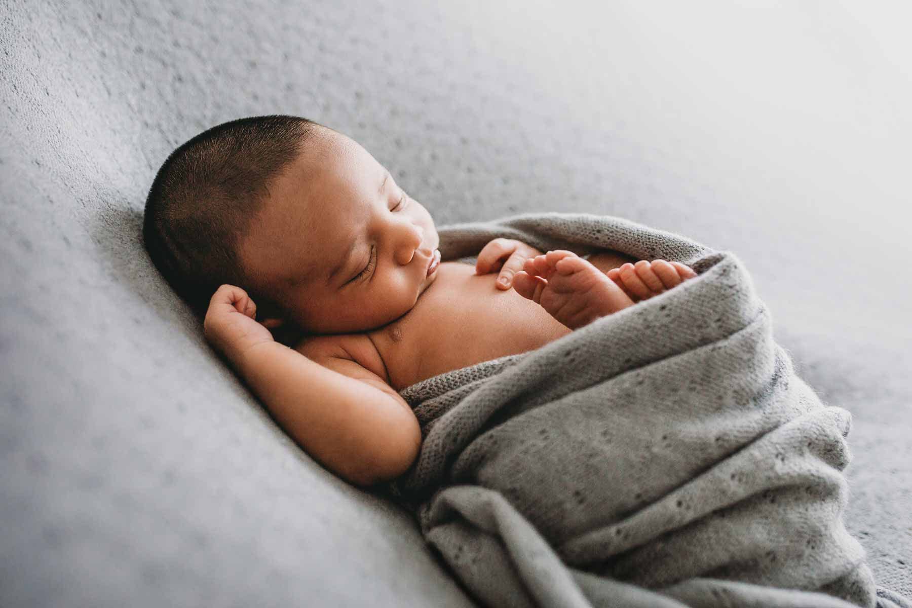 A newborn baby boy posed sleeping wrapped on a grey backdrop