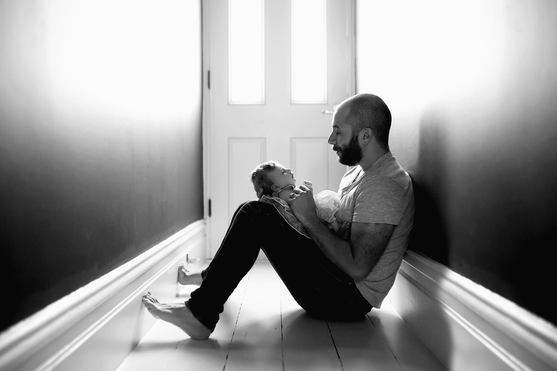 A father holds his newborn baby girl in his lap, sitting in a hallway