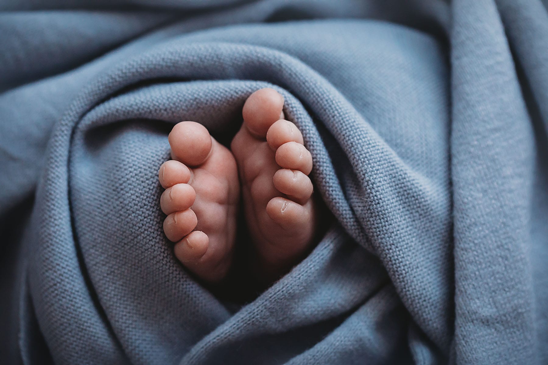 Newborn baby toes poke out from underneath a blue blanket