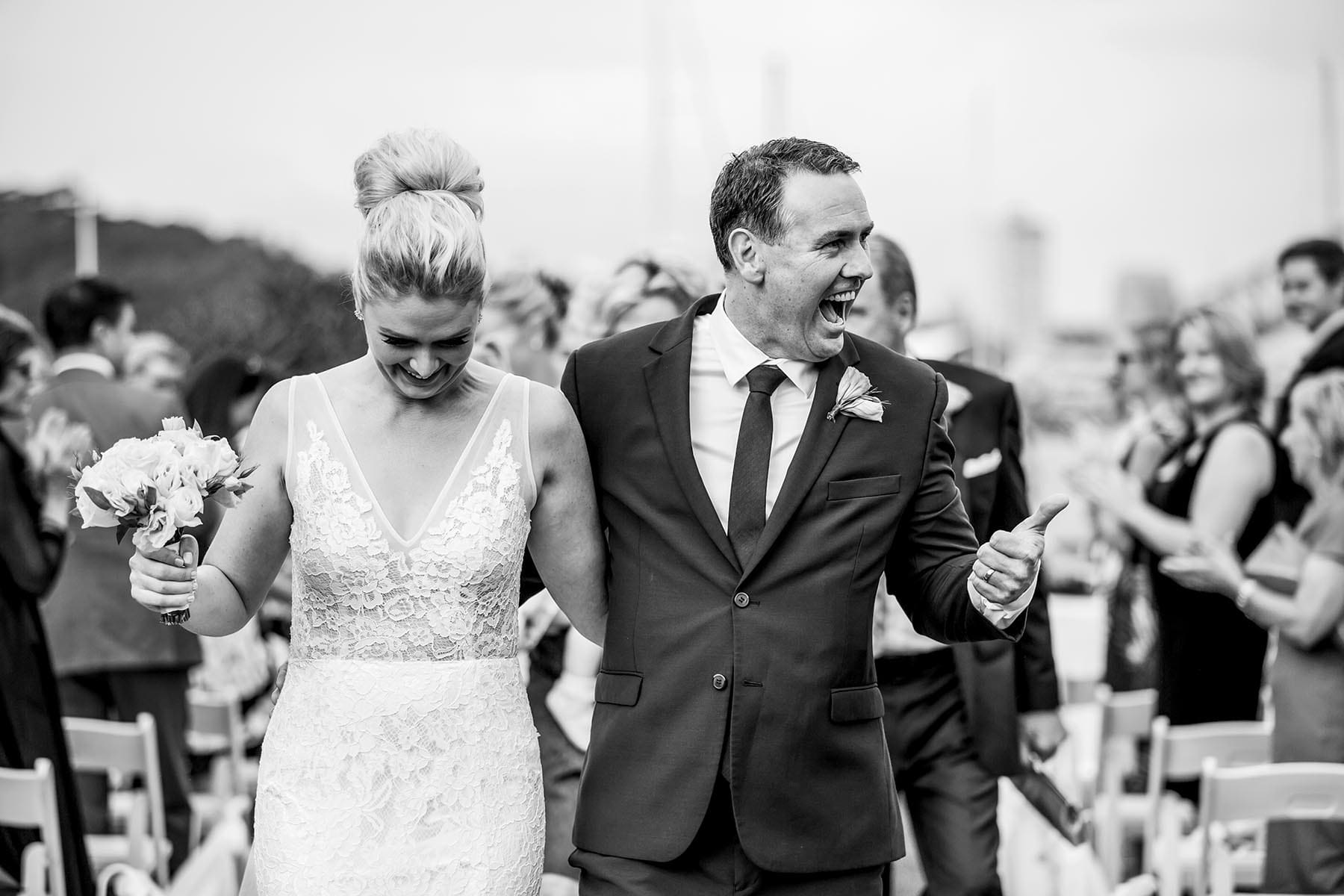 A groom gives their guests a thumbs up walking back down the aisle after the wedding