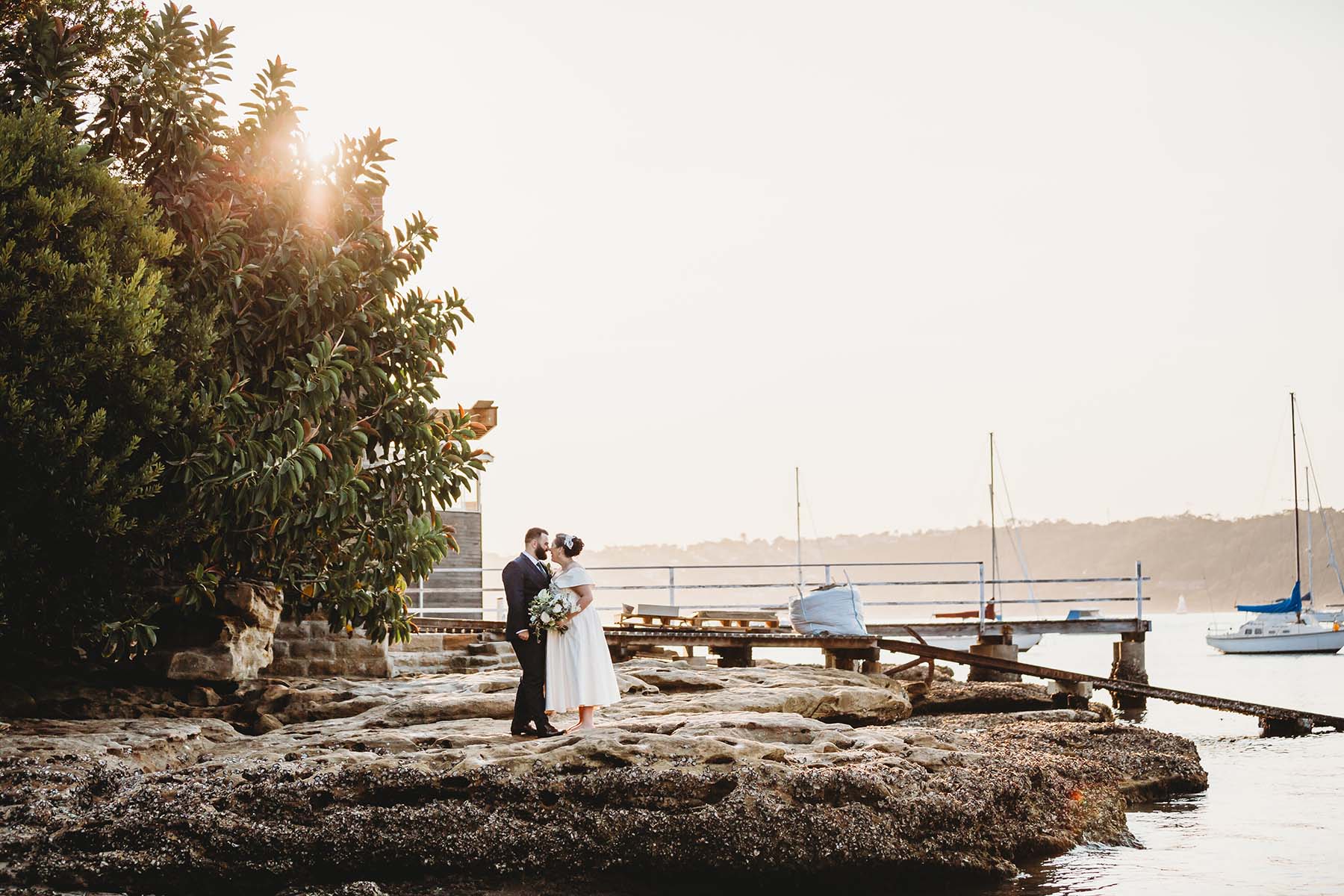 Sydney-Wedding-Photographer-Elysium-Photography-4 Married couple stand cuddling on beach rocks after their Dunbar House wedding