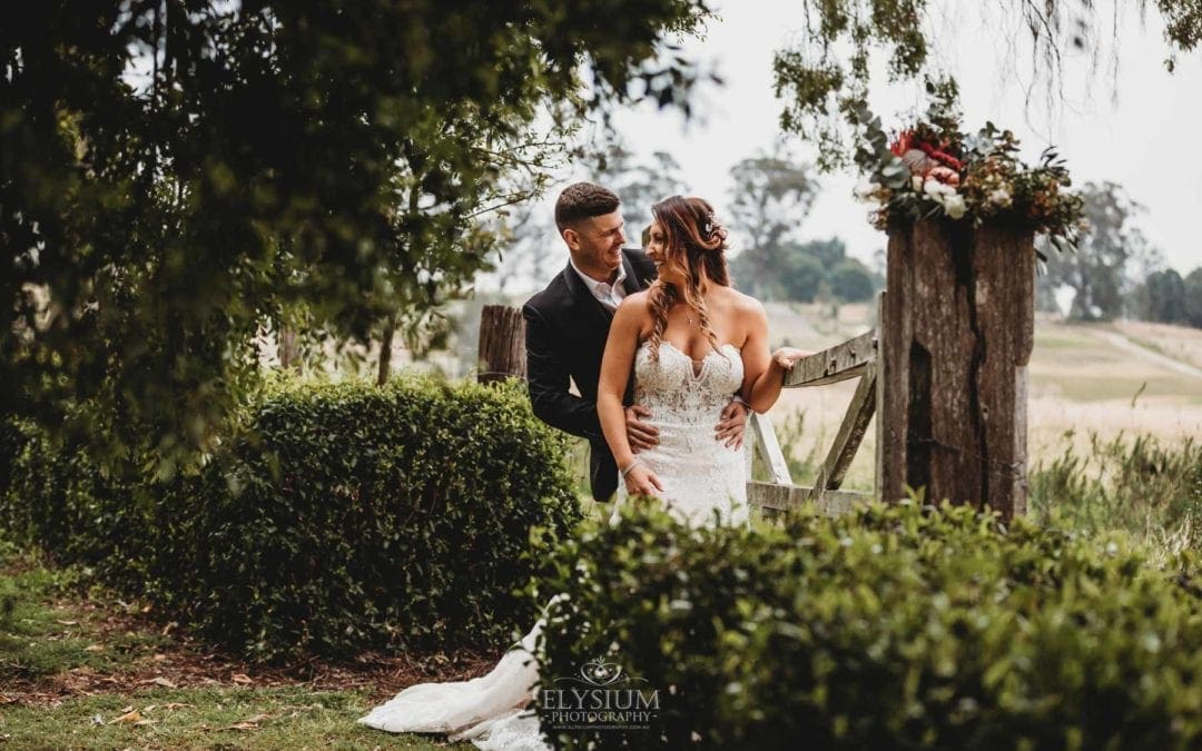 Bride and groom stand at a rustic gate, hugging and sharing a laugh