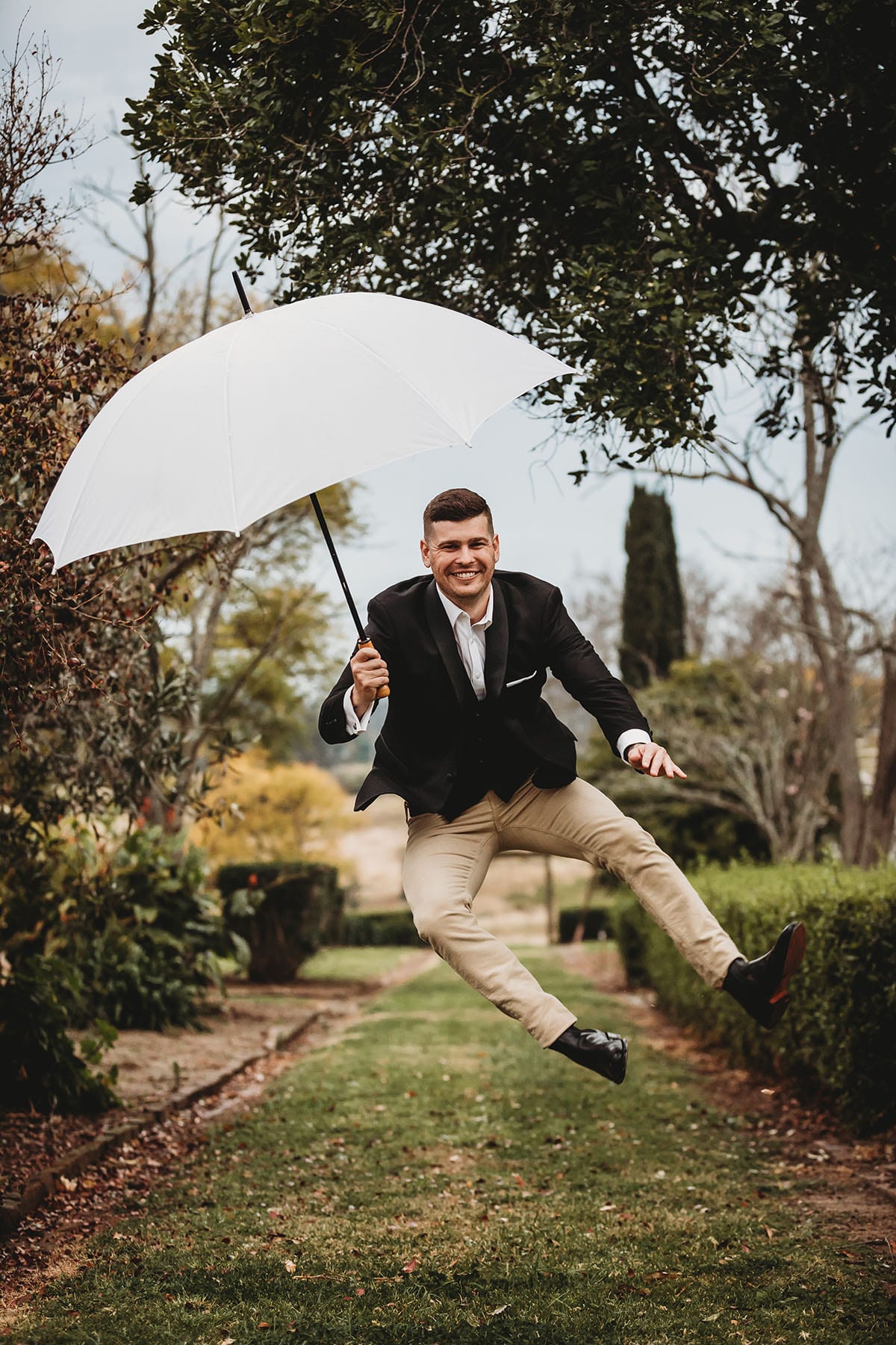 A groom holding an umbrella jumps for joy after the wedding ceremony at Gledswood Estate