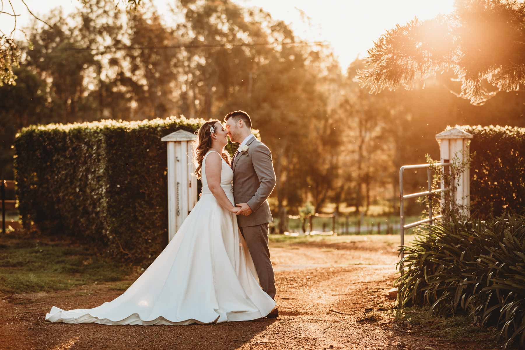 Newlyweds share a tender kiss as they stand on Gledswood Homestead driveway at sunset