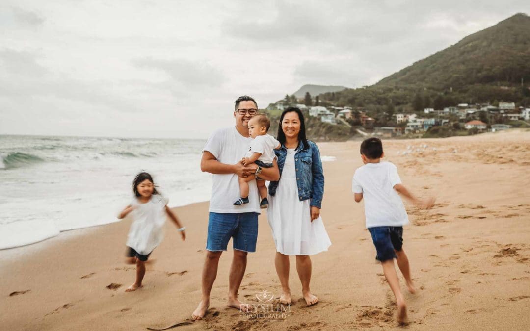 2 children race around their parents while standing on a beach