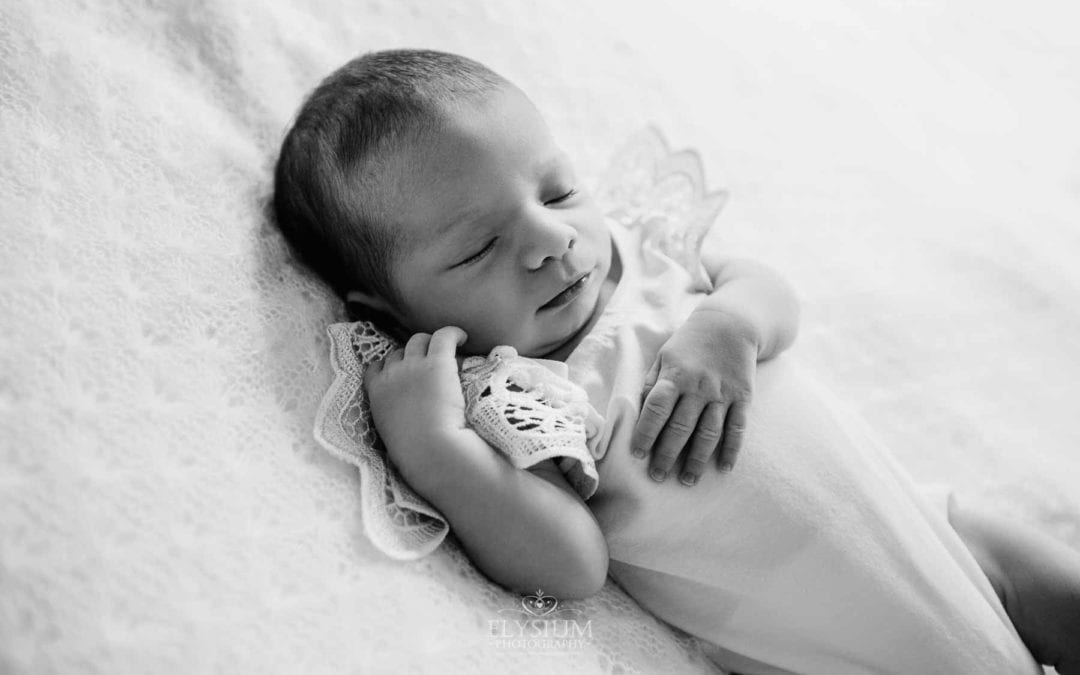 Newborn session - A baby sleeping on her back laying on a white blanket