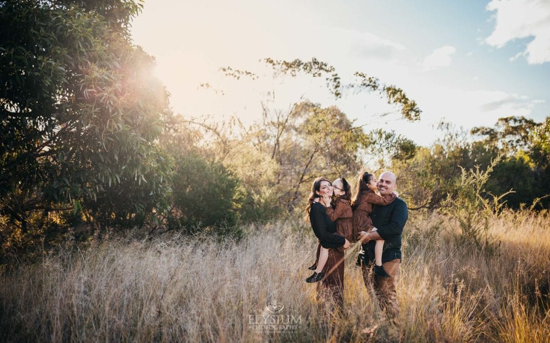 Family Photographer - parents hug their daughters as they stand in a grassy field