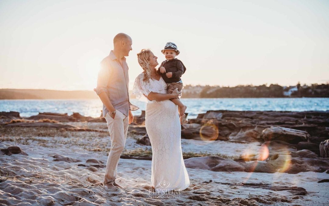 Maternity session - parents hold their boy standing on a beach at sunset
