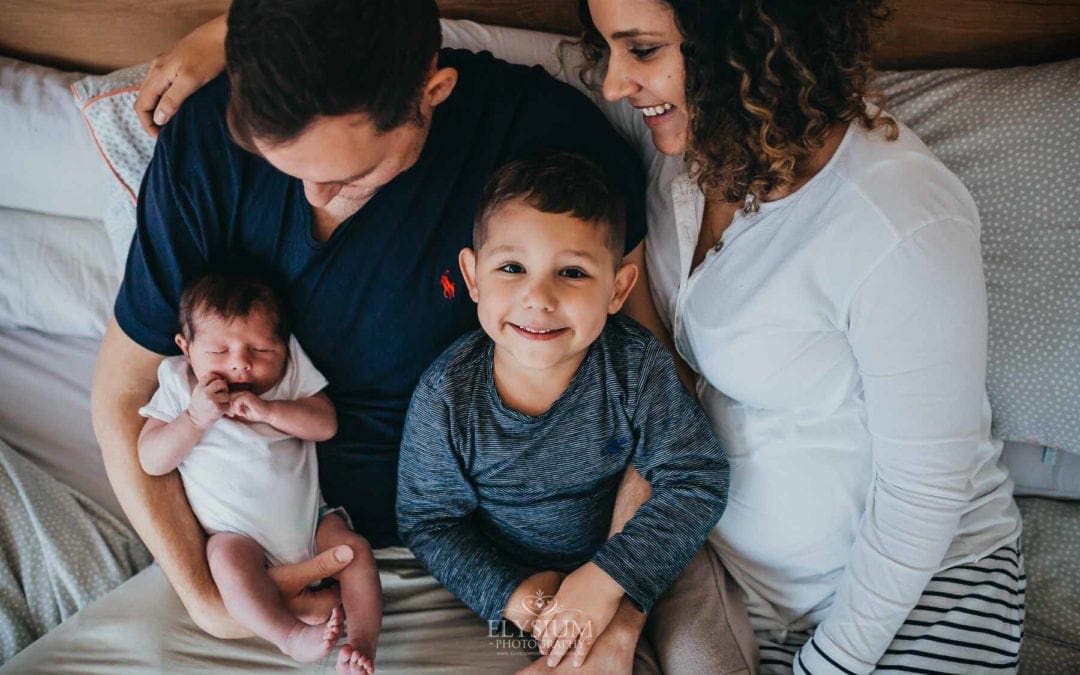 Newborn session - a family sit on a bed with their new baby