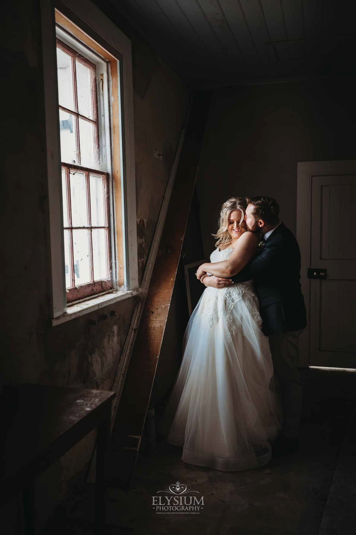 Gledswood Wedding Photo - groom kisses his bride standing at a window