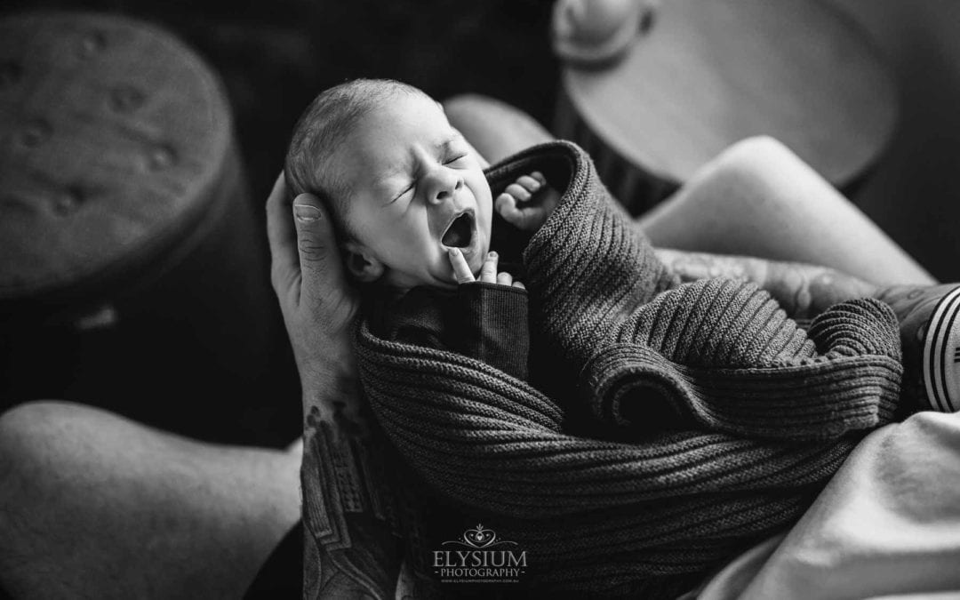 Newborn Photograph - a baby yawns while held in his fathers hands