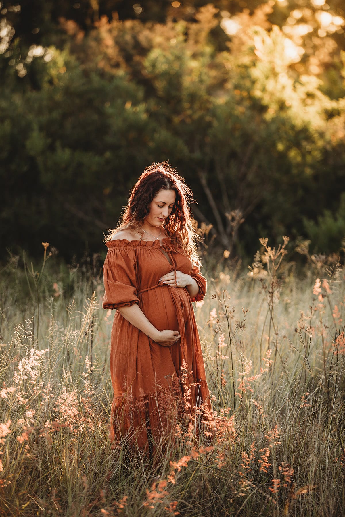 Maternity Photography - a pregnant woman stands in a grassy field at sunset