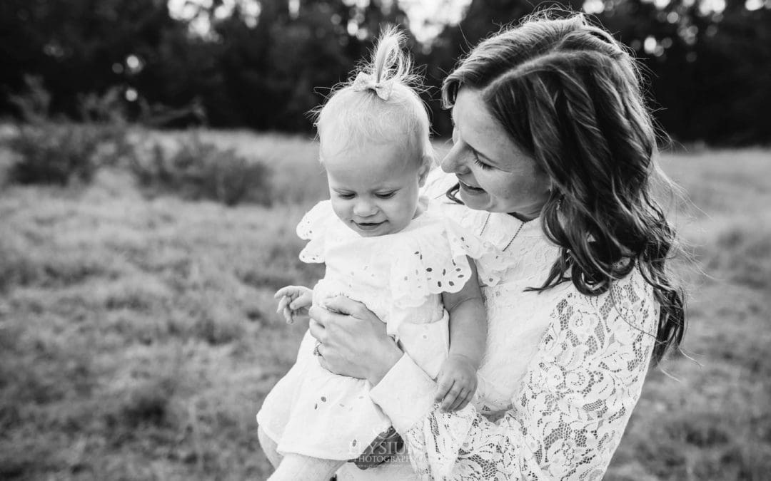 A mother hugs her baby girl in a field at sunset