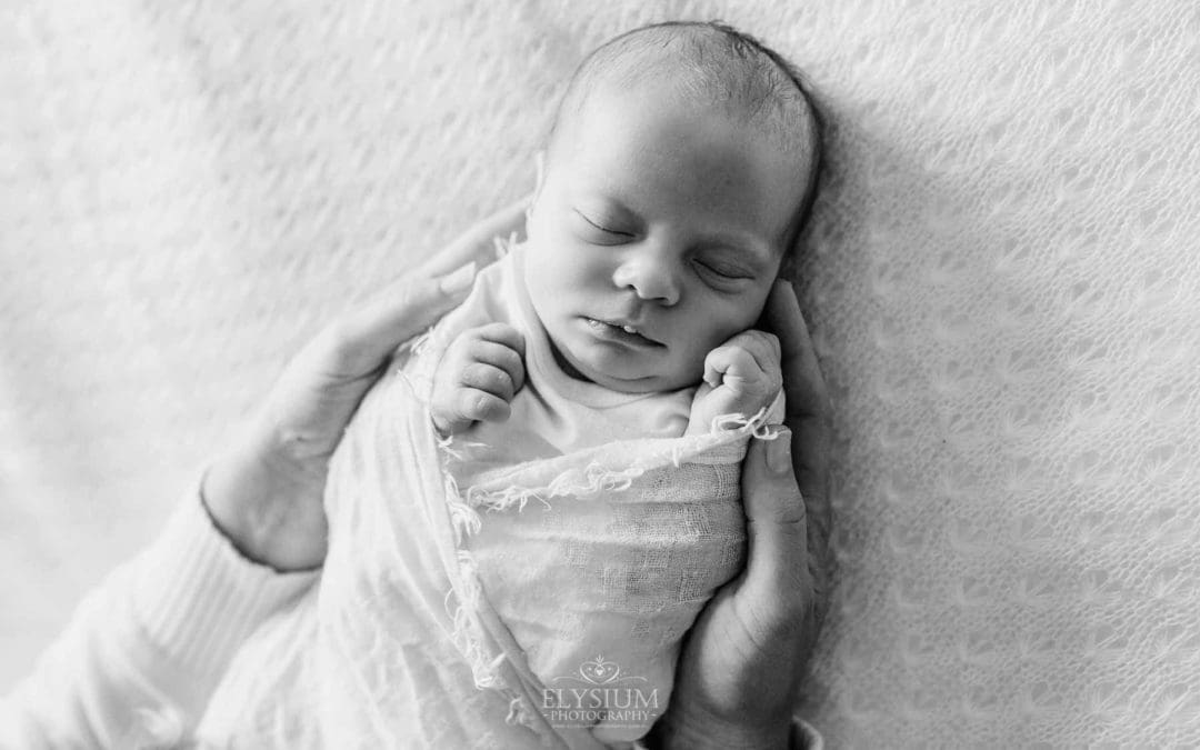 A newborn in a white wrap, mothers hands hold her baby