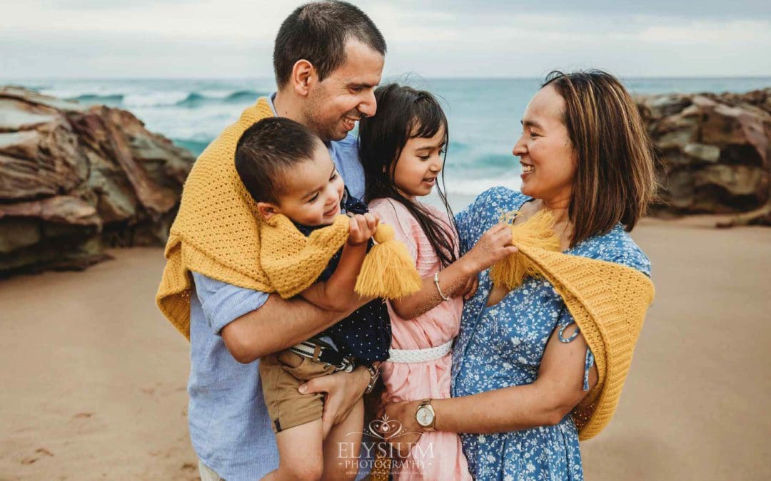 Parents cuddle their children between them wrapped in a yellow blanket