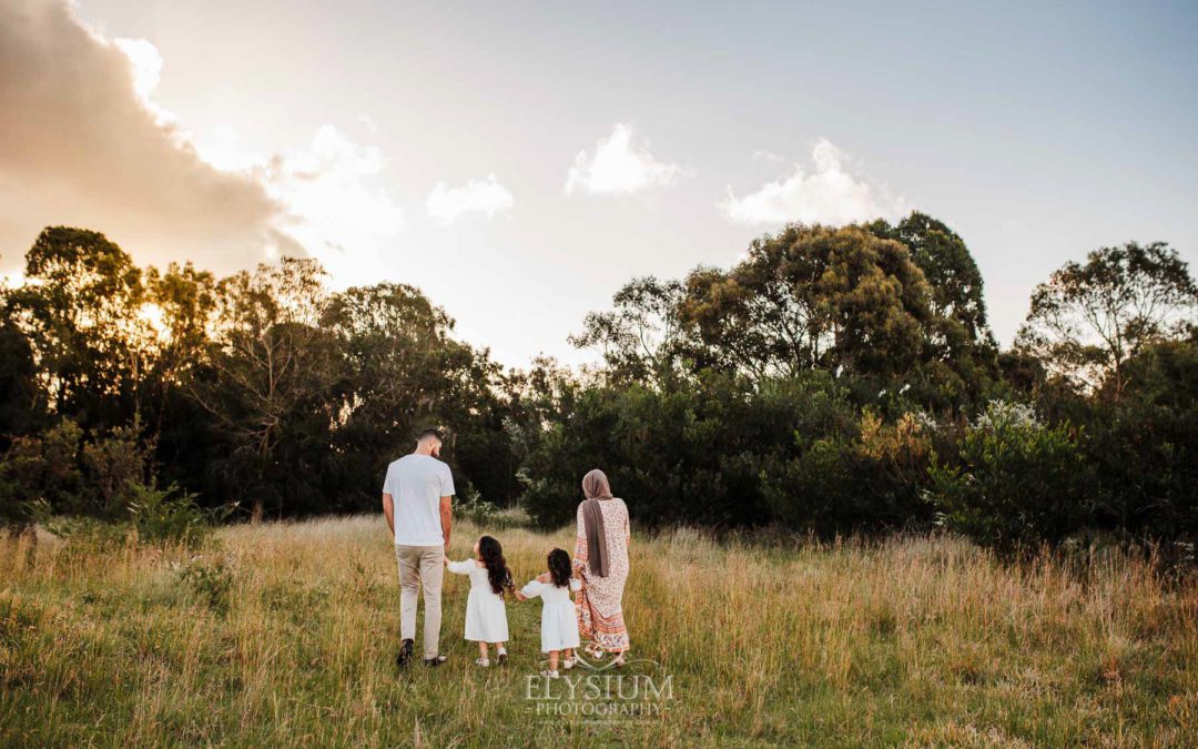 A family walk through a grass field holding hands at sunset