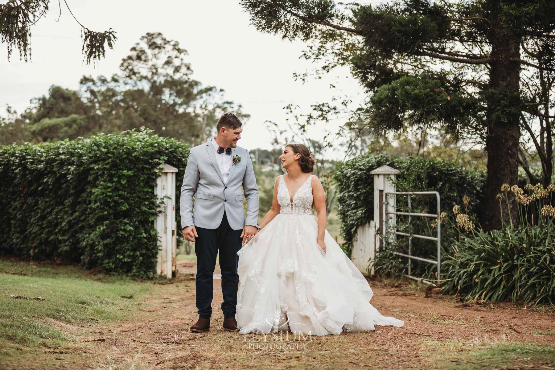Gledswood Wedding - a bride and groom hold hands standing on a dirt driveway at the venue