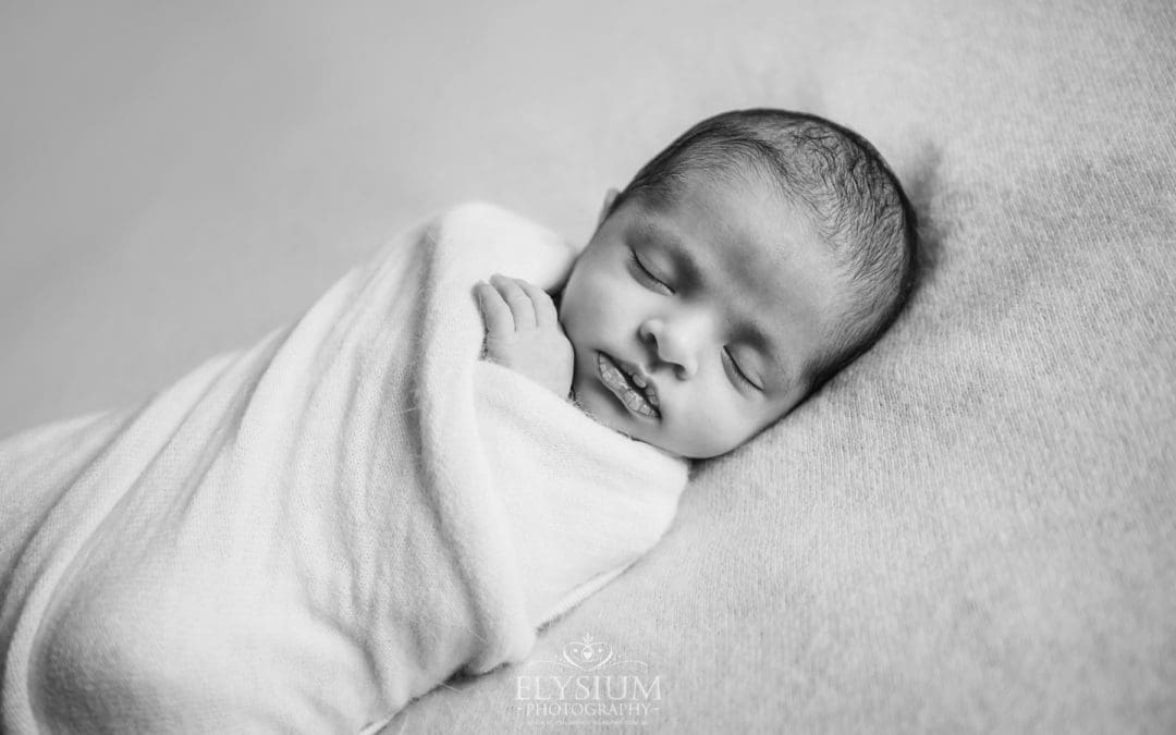 A tiny newborn lays on a white blanket in a white wrap