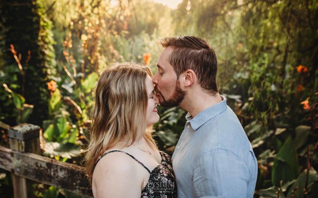 A man kisses his fiancée on the forehead as they stand on a boardwalk