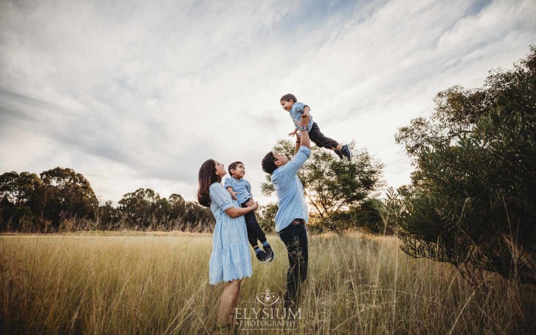 Family Session - a father hoists his son into the air in a grassy field at sunset