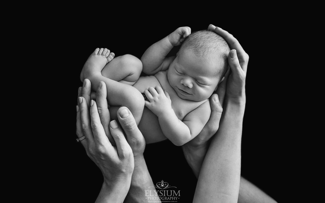 Newborn Photography: a baby boy smiles as he sleeps in his parents hands