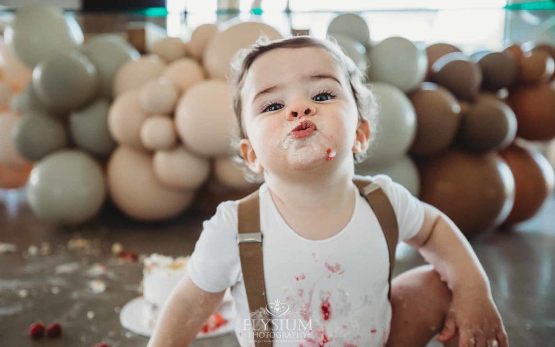 Cake Smash Photographer: a baby boy sits covered in icing pulling faces