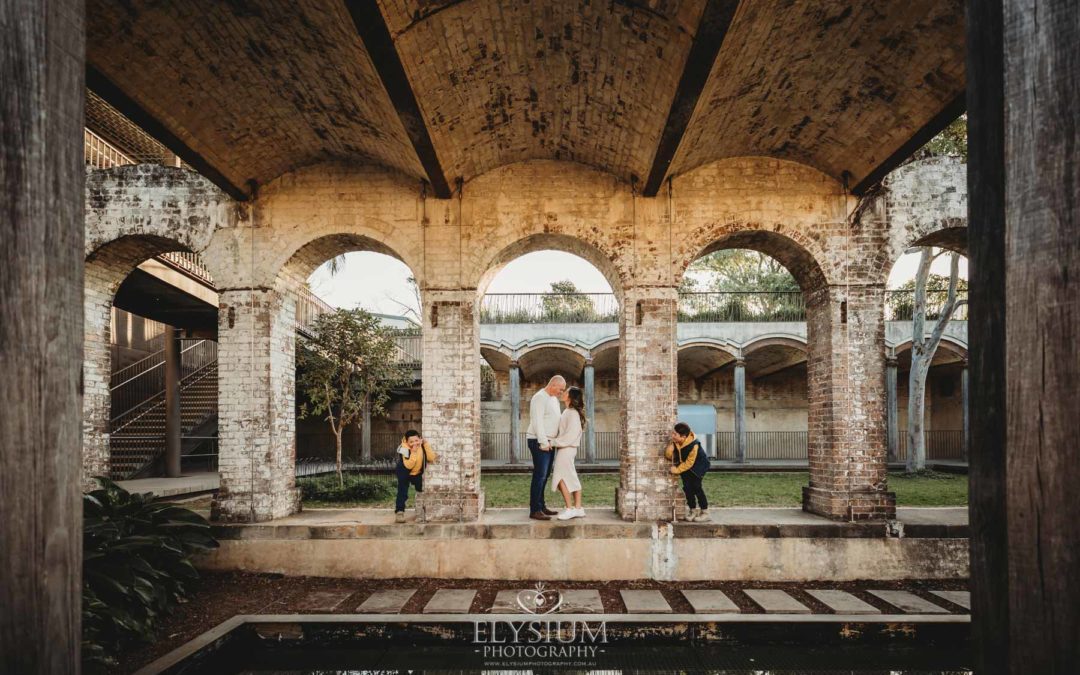 Sydney Family Photographer: parents kiss as their kids giggle under a rustic brick arch
