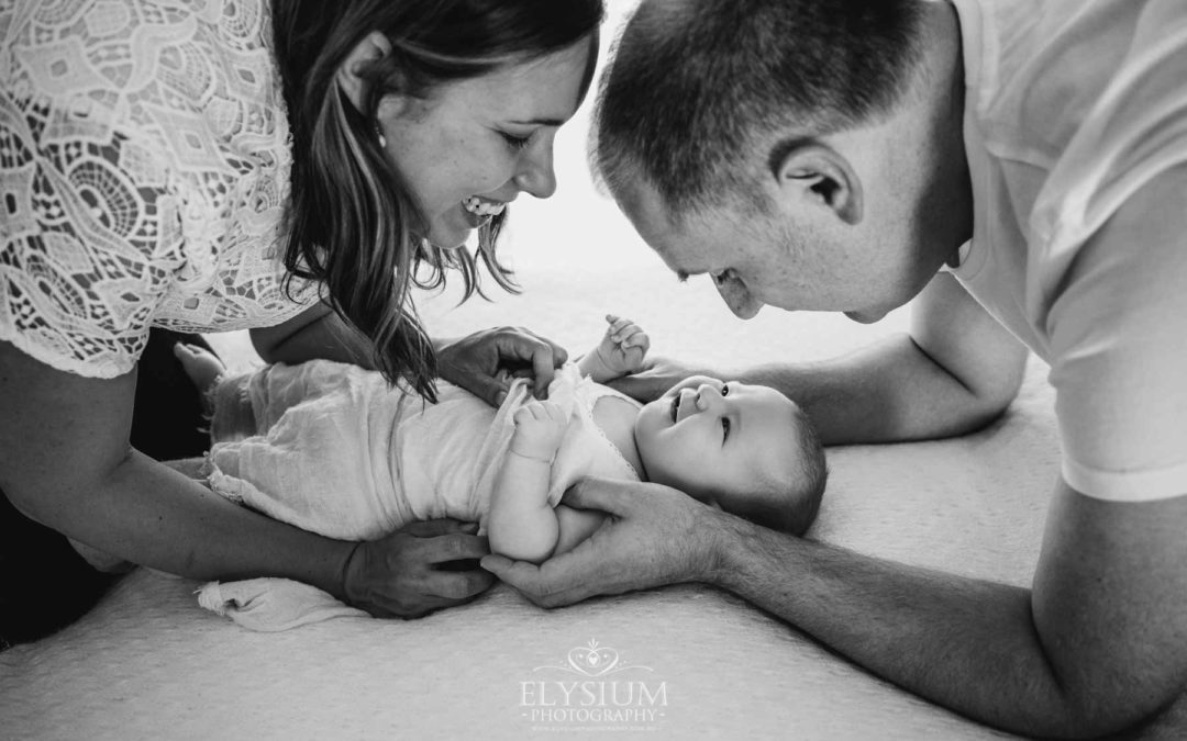Parents hold their baby girl between them on a bed