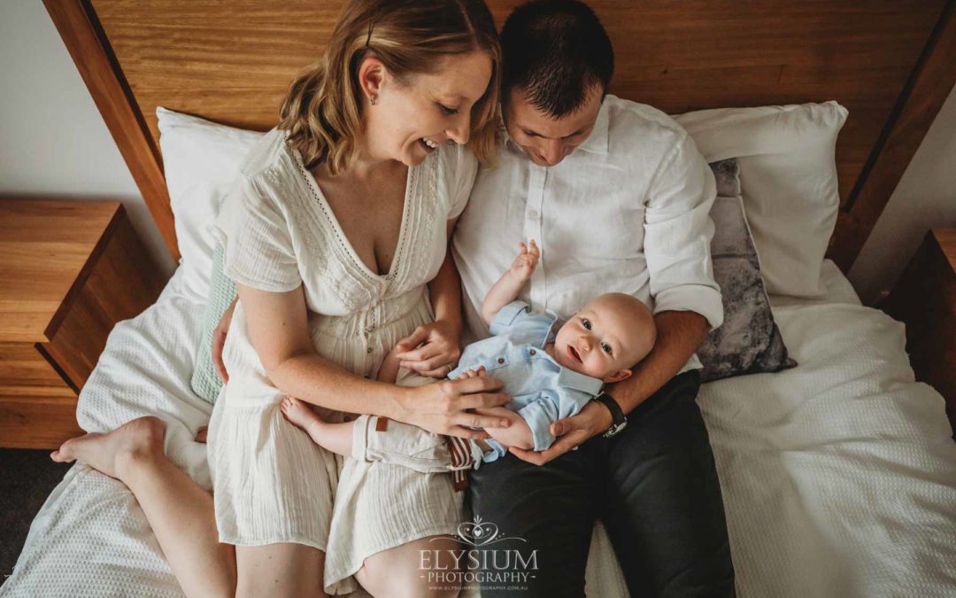 Newborn Photographer: parents sitting on a bed with their baby boy