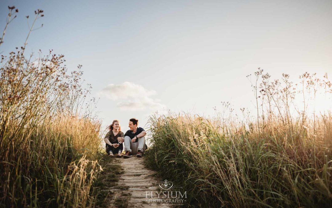 Engagement Photographer: a couple sit on a dirt path surrounded by long grass