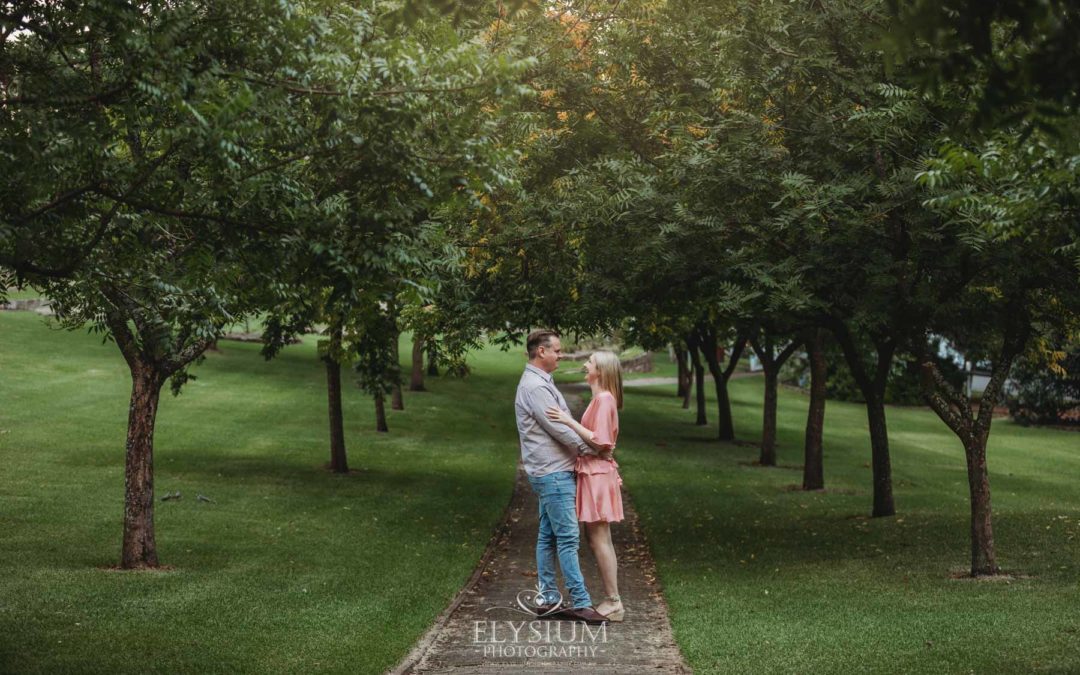 Engagement Photography: a couple stand hugging on a path through leafy green trees