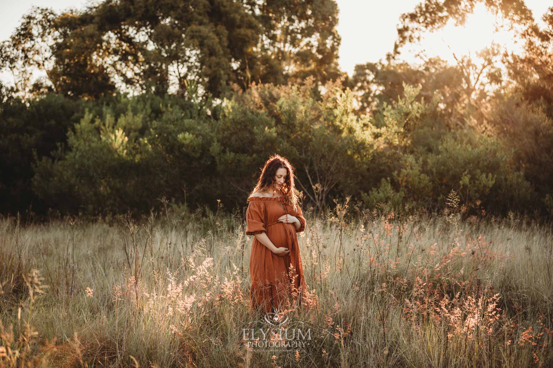 Outdoor Session - a woman wearing a long rust maternity dress holds her pregnant belly