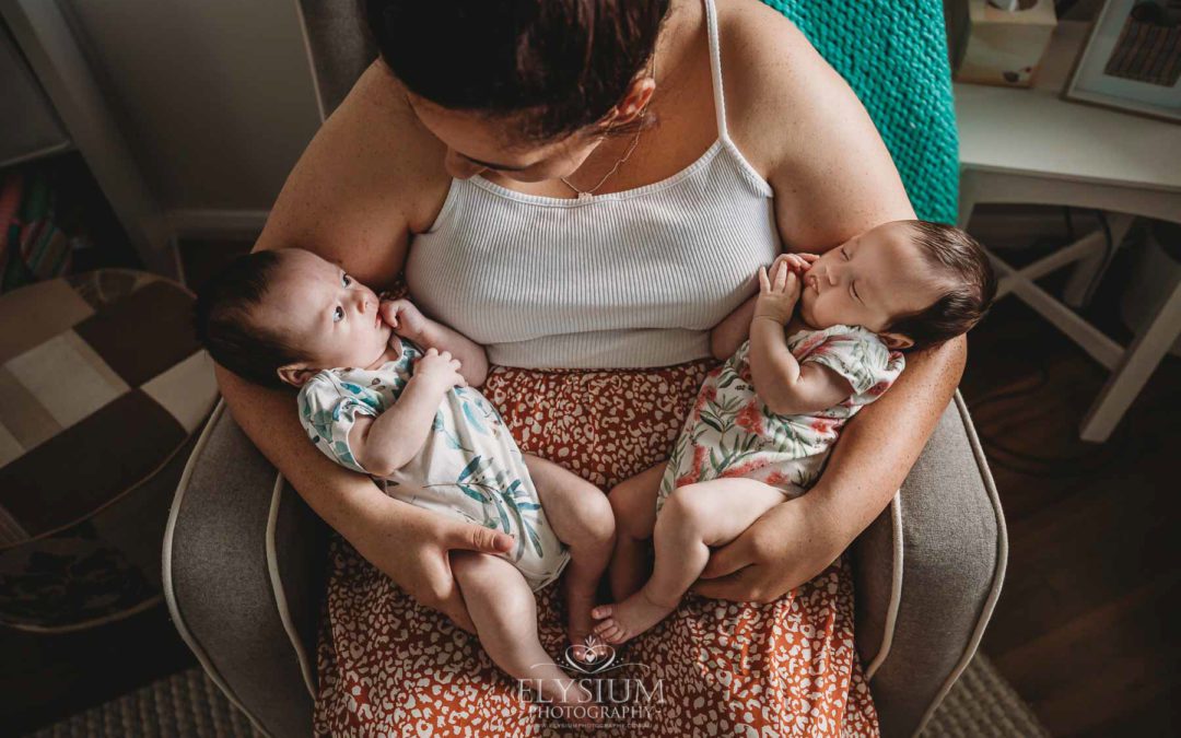 A mother sits in a chair holding her newborn twins in her arms