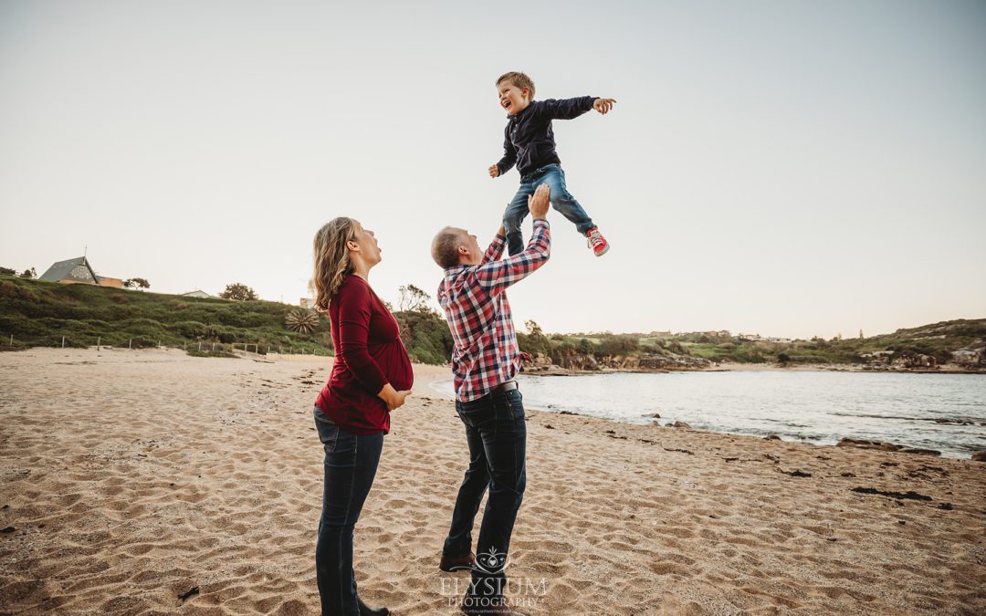 A little boy is tossed in the air by his dad as his pregnant mum watches on
