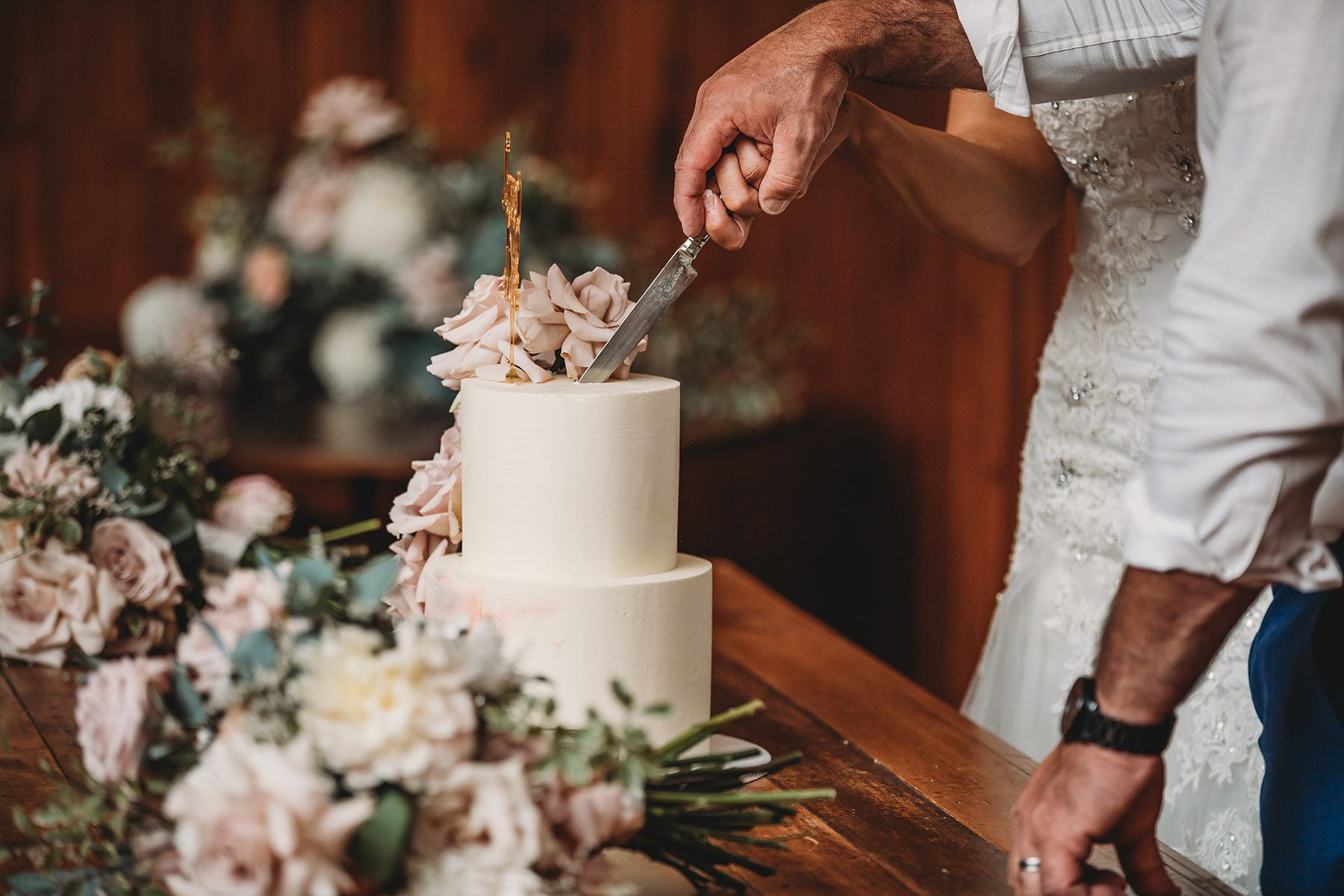 A couple hold hands as they cut into their wedding cake