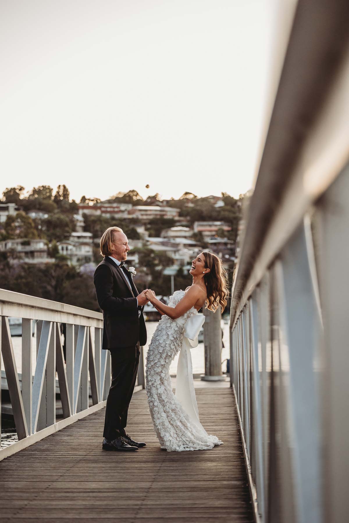 Bride and groom stand on a wharf laughing after their wedding ceremony on Sydney harbour