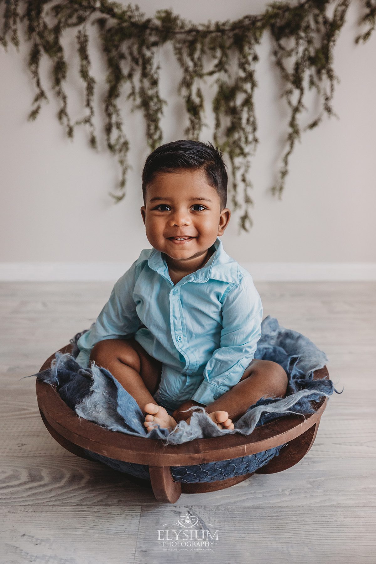 A smiley baby boy wearing blue sits in a wooden bowl