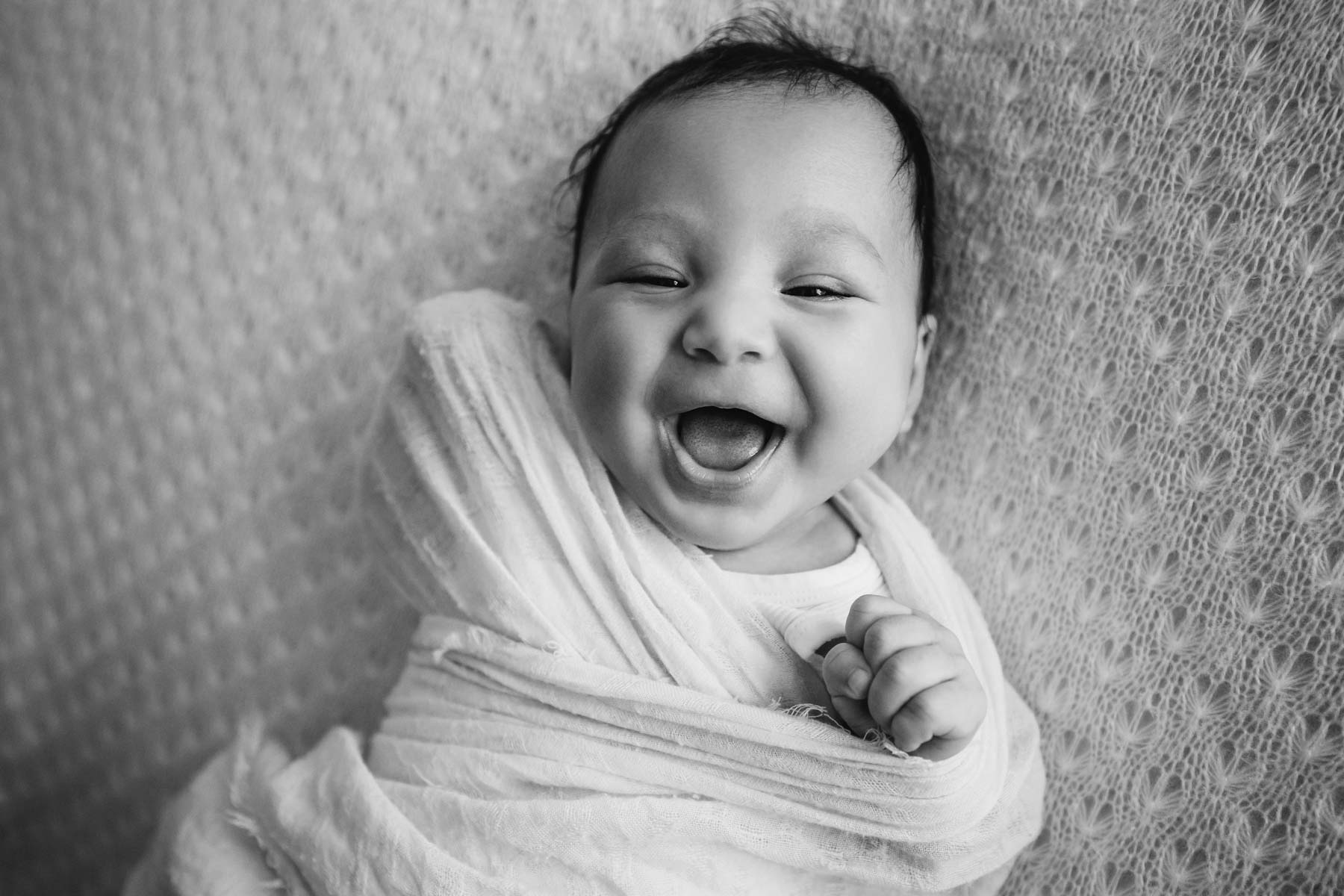 A baby boy smiles as he lays on a white rug
