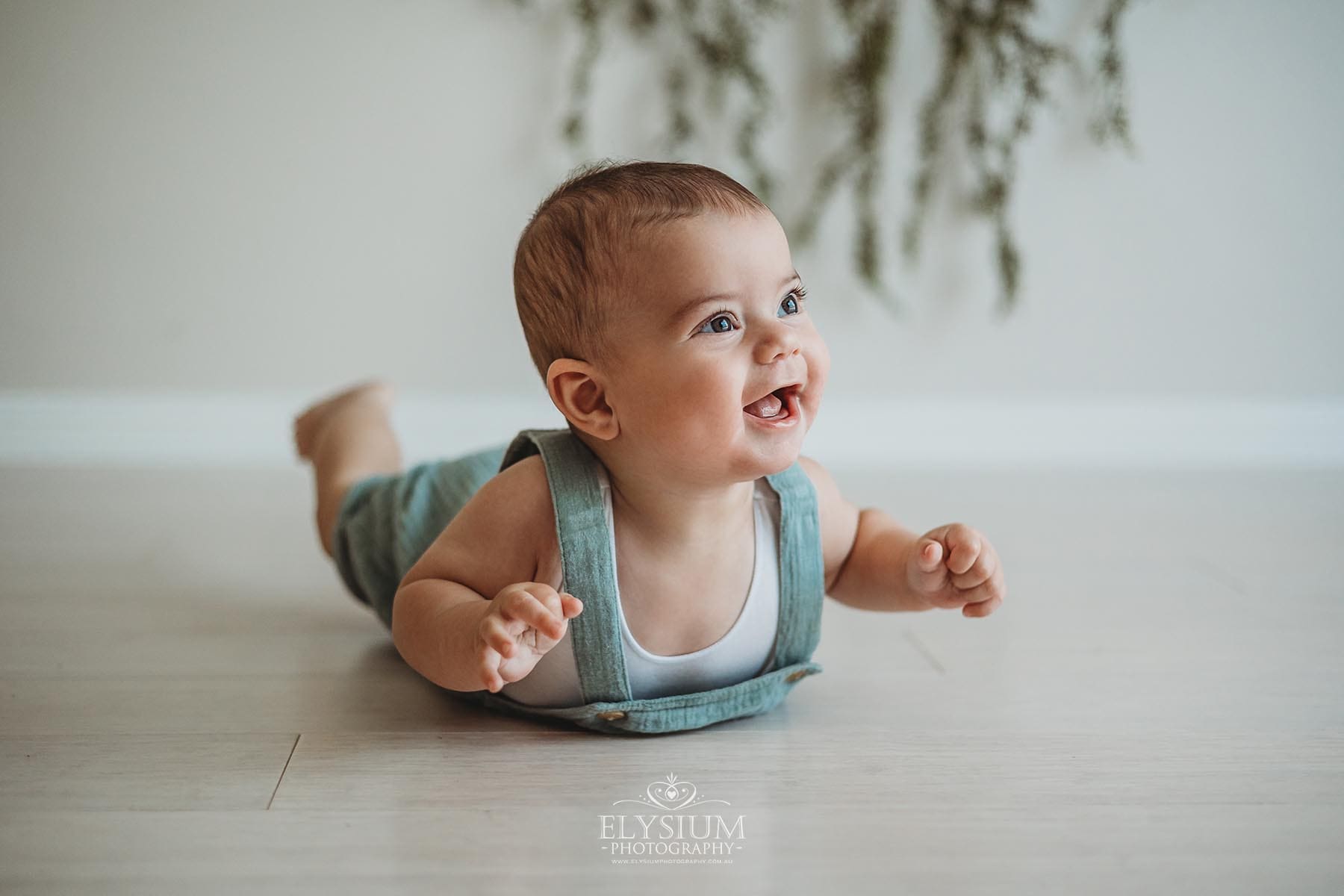 A baby lays on his tummy and smiles in a bright studio