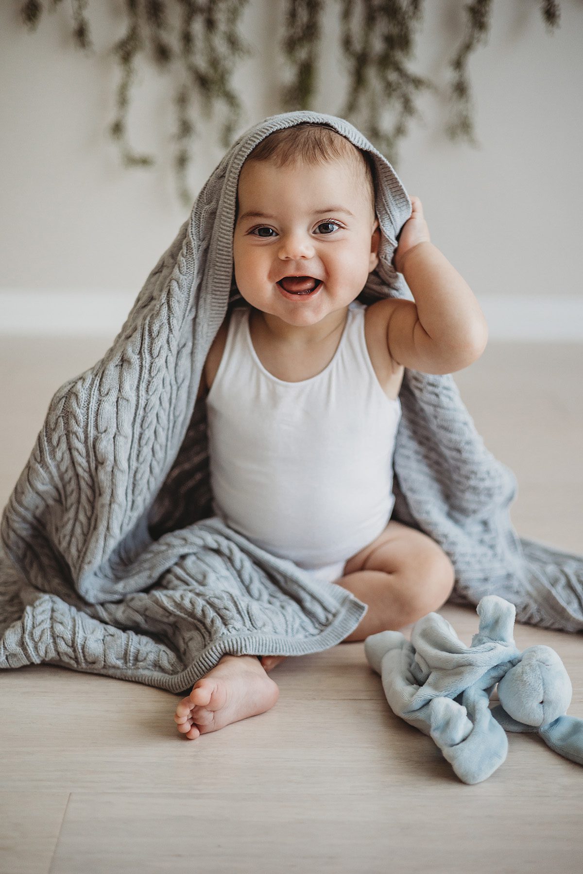 A baby smiles as he plays peekaboo under a grey blanket